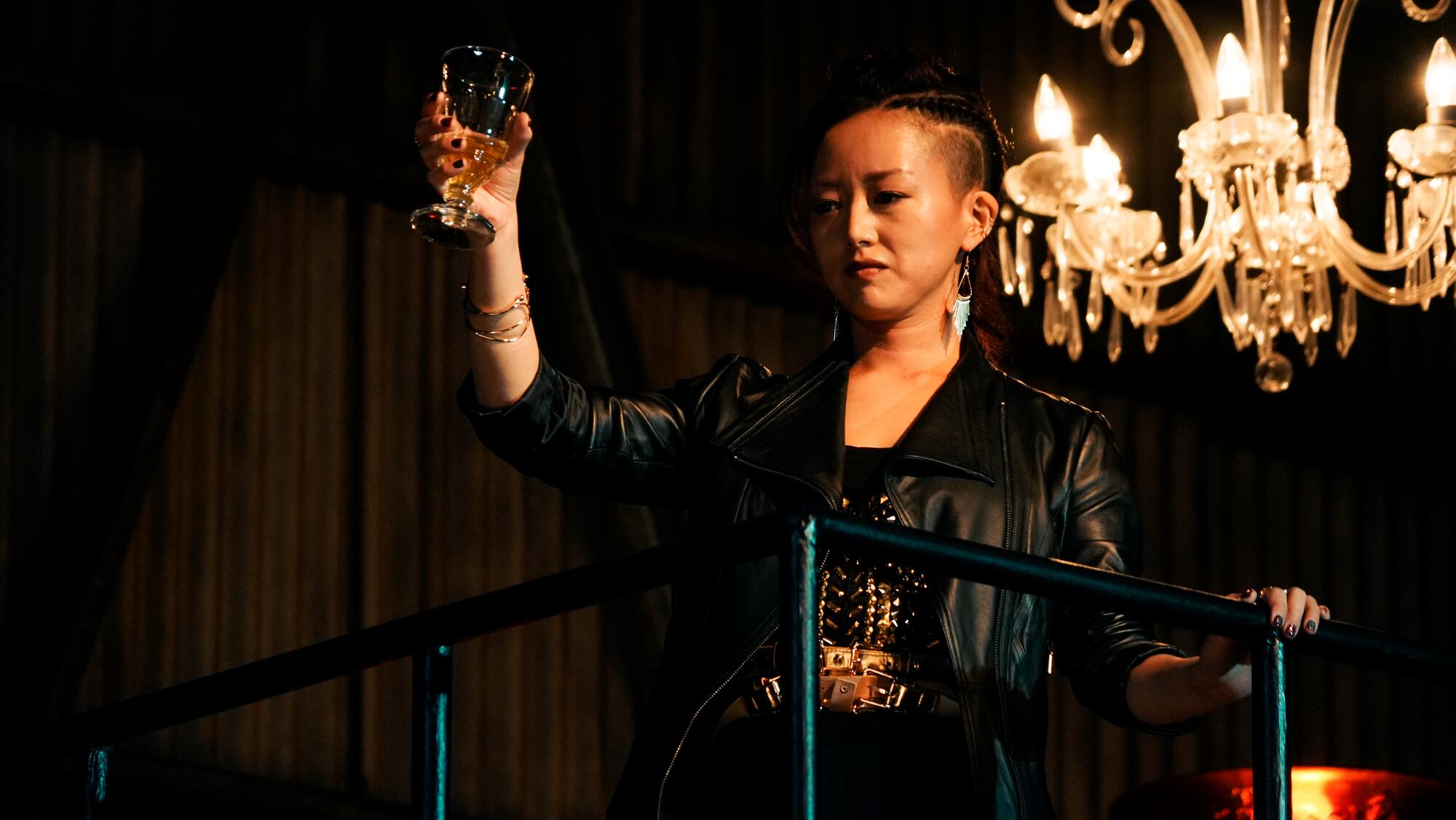 Kaori raising a glass beneath a chandelier